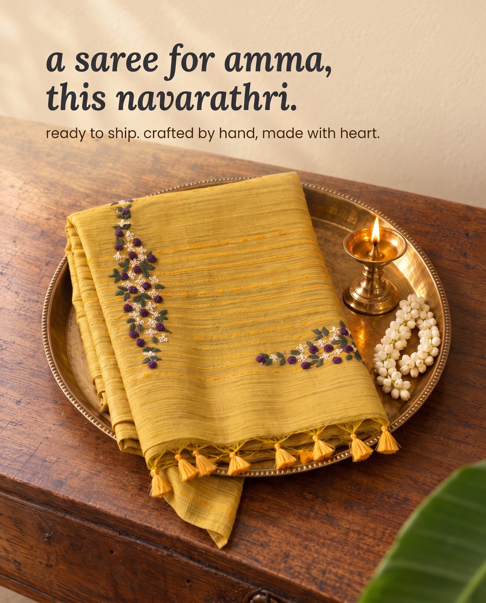 A folded saree on a brass tray with jasmine and a small lamp